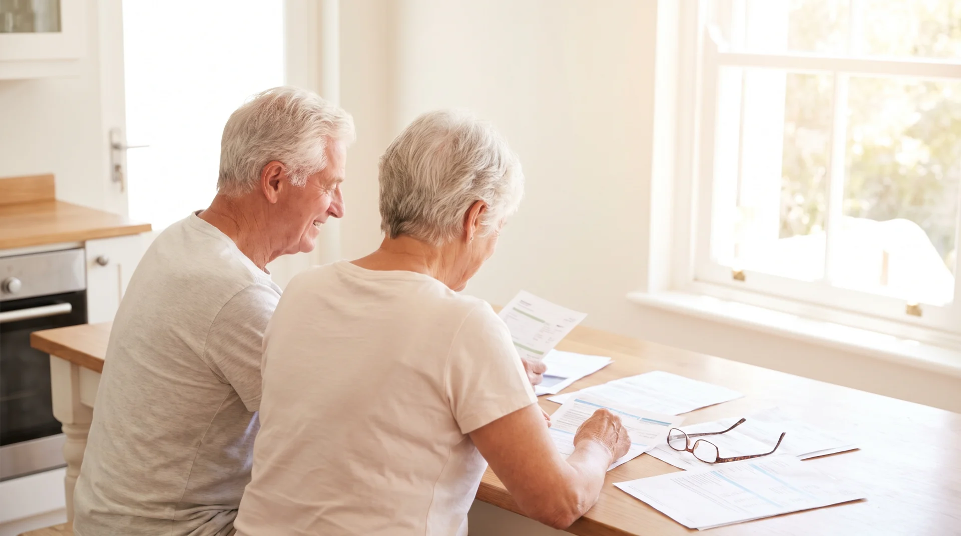 Couple de seniors examinant des documents à une table de cuisine ensoleillée